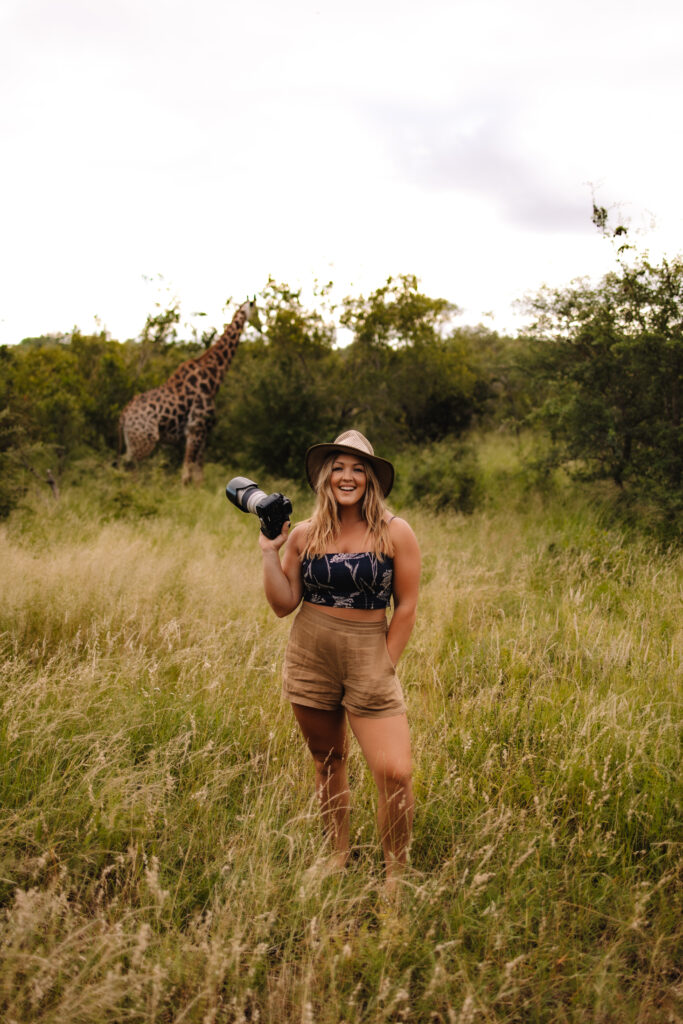 Safari wedding and elopement photographer headshot in the bush with a giraffe in the background