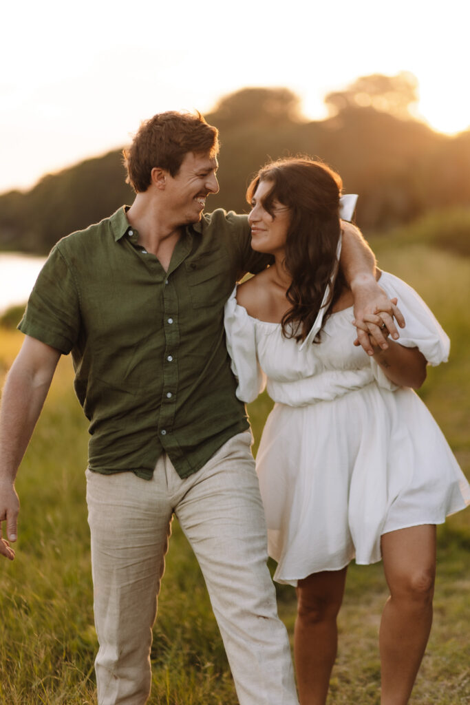 Guy with his arm around his girl walking together happily during their engagement session in Minneapolis' west suburbs- Excelsior beach