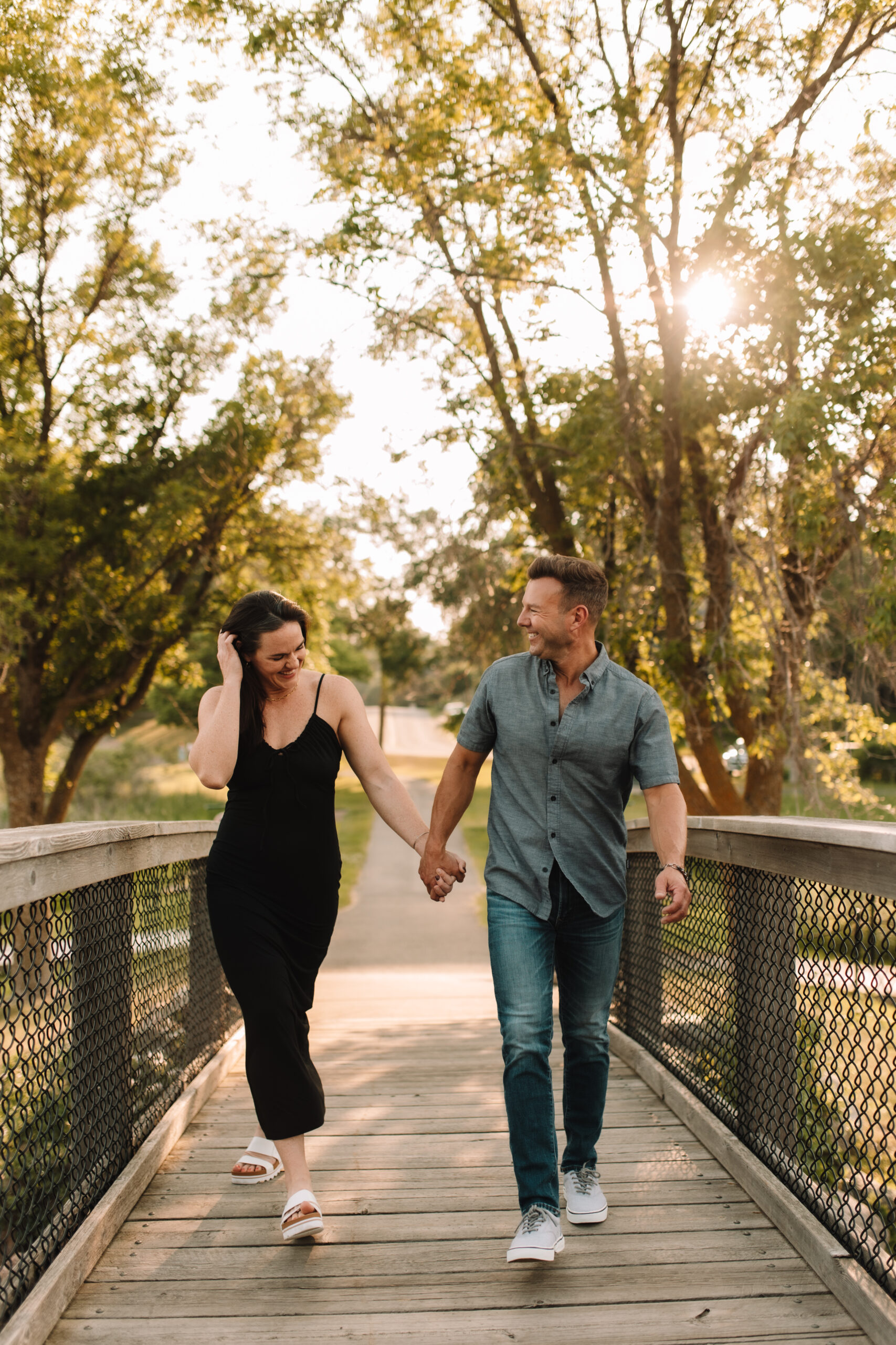 Guy and girl walking across a bridge laughing during their engagement session at Wayzata Beach- one of the best engagement photo locations in Minneapolis' west suburbs