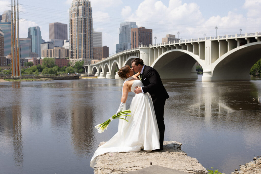Groom dip kissing his Bride at St. Anthony Main before the ceremony at The View, in front of the Minneapolis skyline