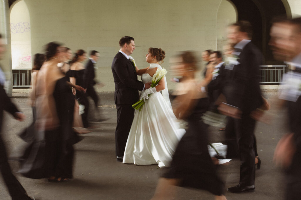 Bride and Groom staring at each other while wedding party runs around them creating a blurry effect