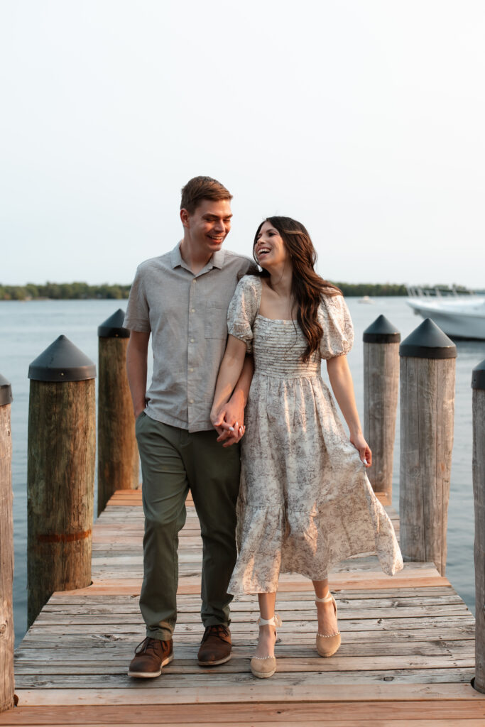 Engagement couple walking hand in hand together, bumping hips and laughing on the docks in Wayzata during their engagement photos