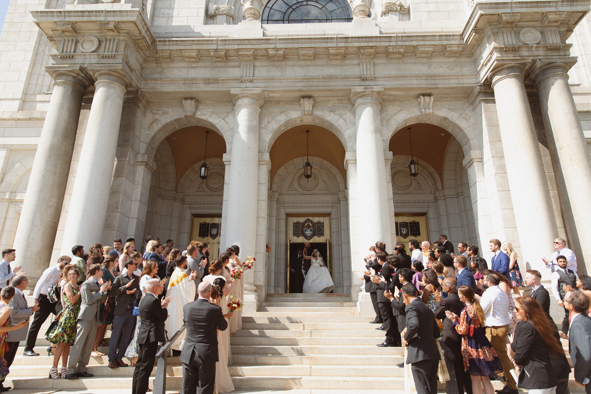 Bride and Groom walking down the stairs after their ceremony while their guests cheer at The Basilica of St. Mary church in Minneapolis