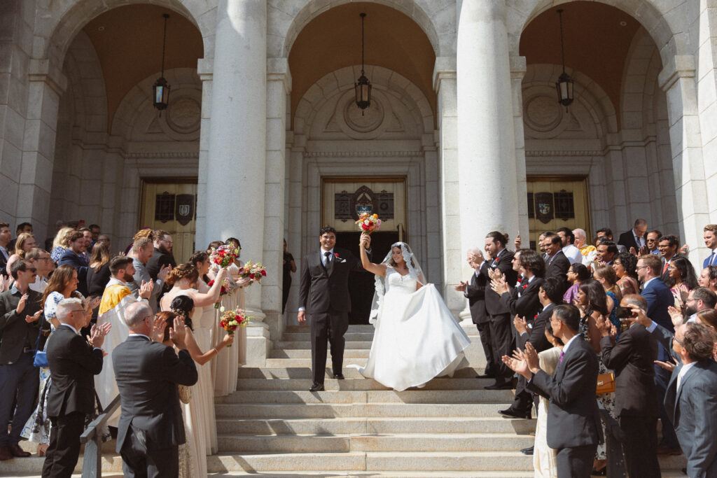 Bride and Groom walking down the stairs after their ceremony while their guests cheer at The Basilica of St. Mary church in Minneapolis