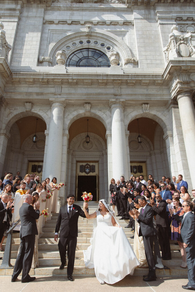 Bride and Groom walking down the stairs after their ceremony while their guests cheer at The Basilica of St. Mary church in Minneapolis