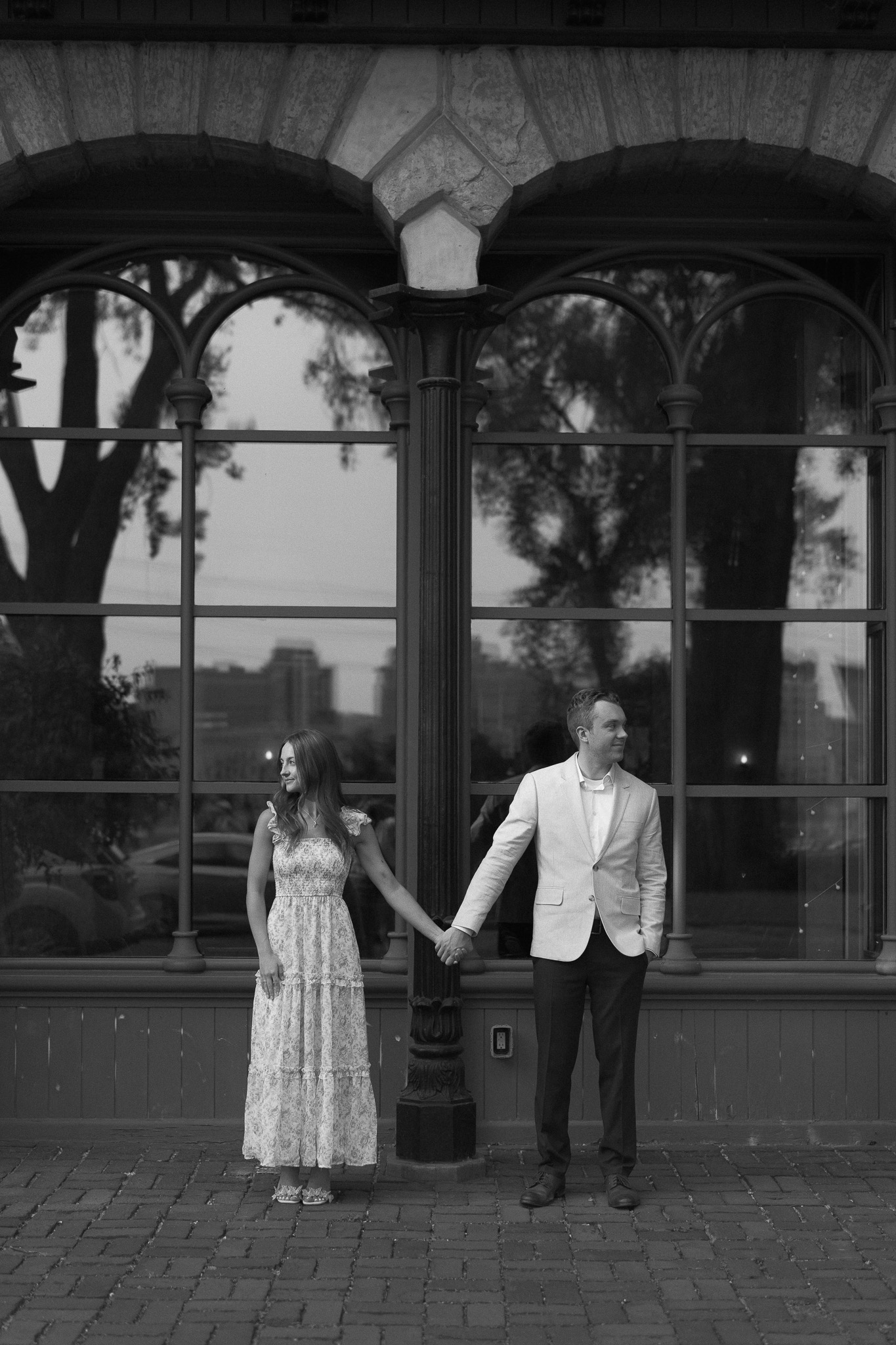 Engagement couple standing next to each other holding hands, in front of the stores in St Anthony Main