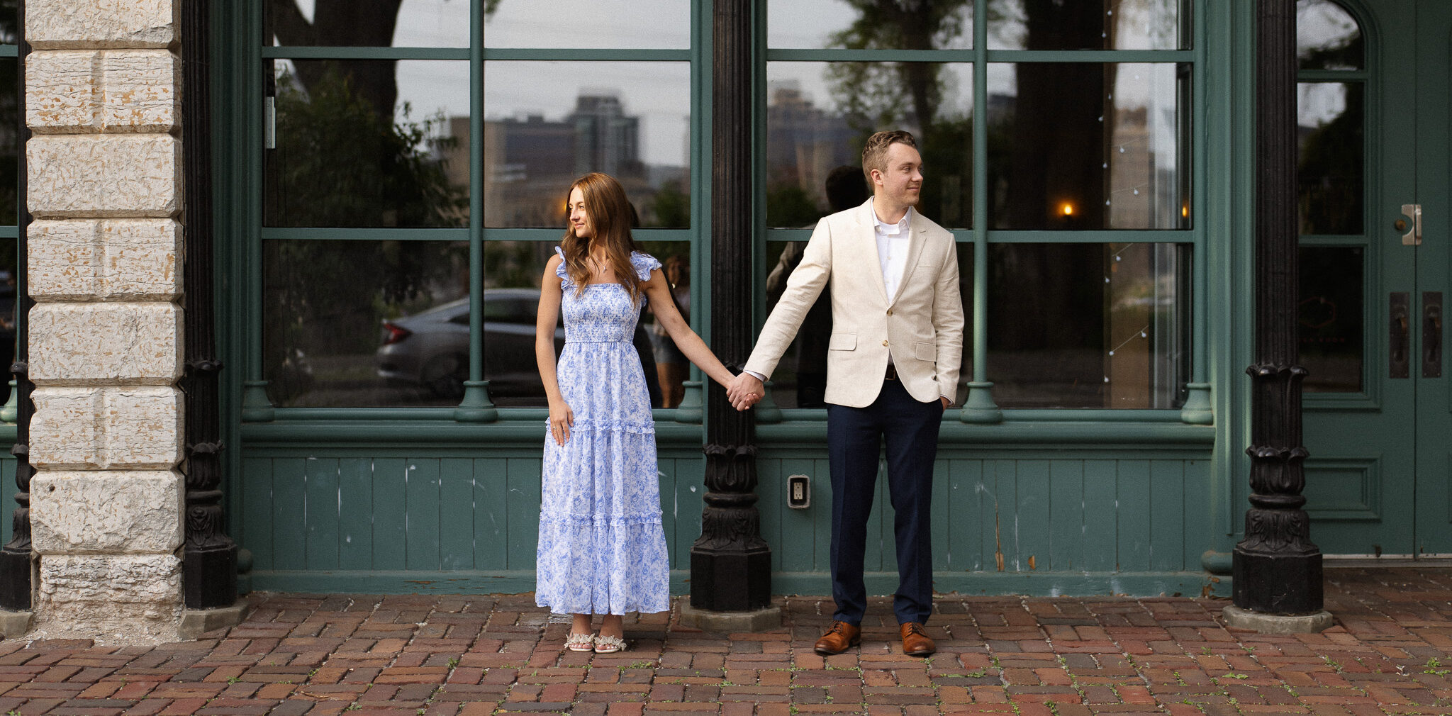 Engagement couple standing next to each other holding hands, in front of the stores in St Anthony Main