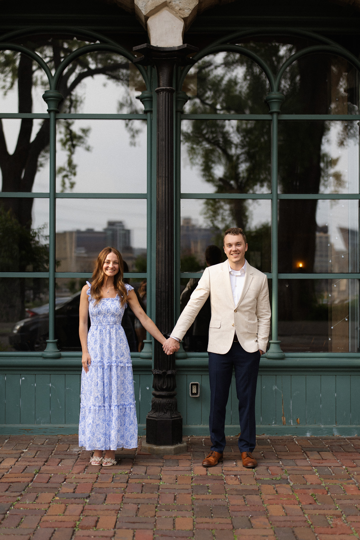 Engagement couple standing next to each other holding hands, in front of the stores in St Anthony Main