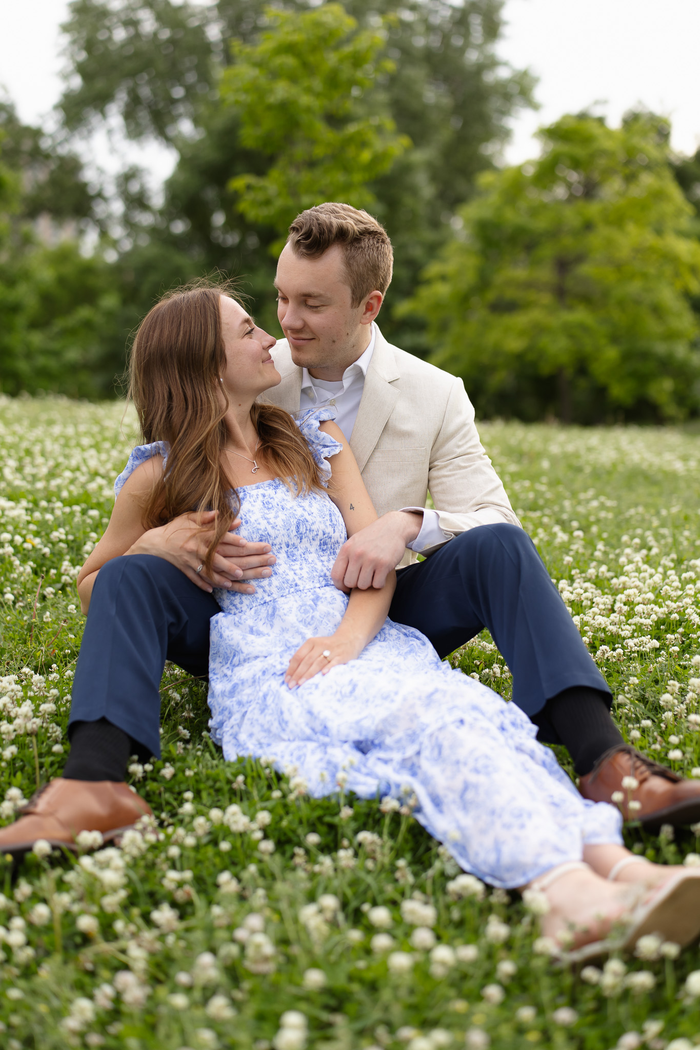 Engagement couple snuggling together on the grass with flowers surrounding them during their Minneapolis engagement session in St Anthony Main