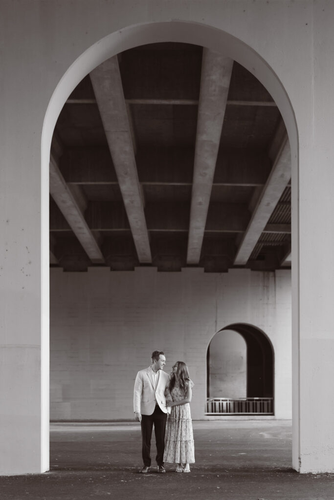 Editorial-style engagement photo of couple standing under the Main Street Bridge in St. Anthony Main, Minneapolis.