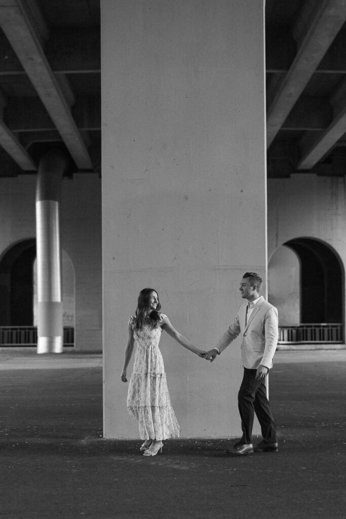 Editorial-style engagement photo of couple walking taken under the Main Street Bridge in St. Anthony Main, Minneapolis.