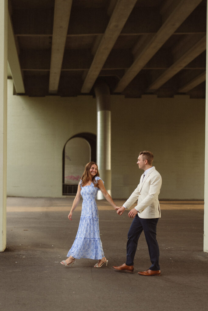 Editorial-style engagement photo of couple walking taken under the Main Street Bridge in St. Anthony Main, Minneapolis.