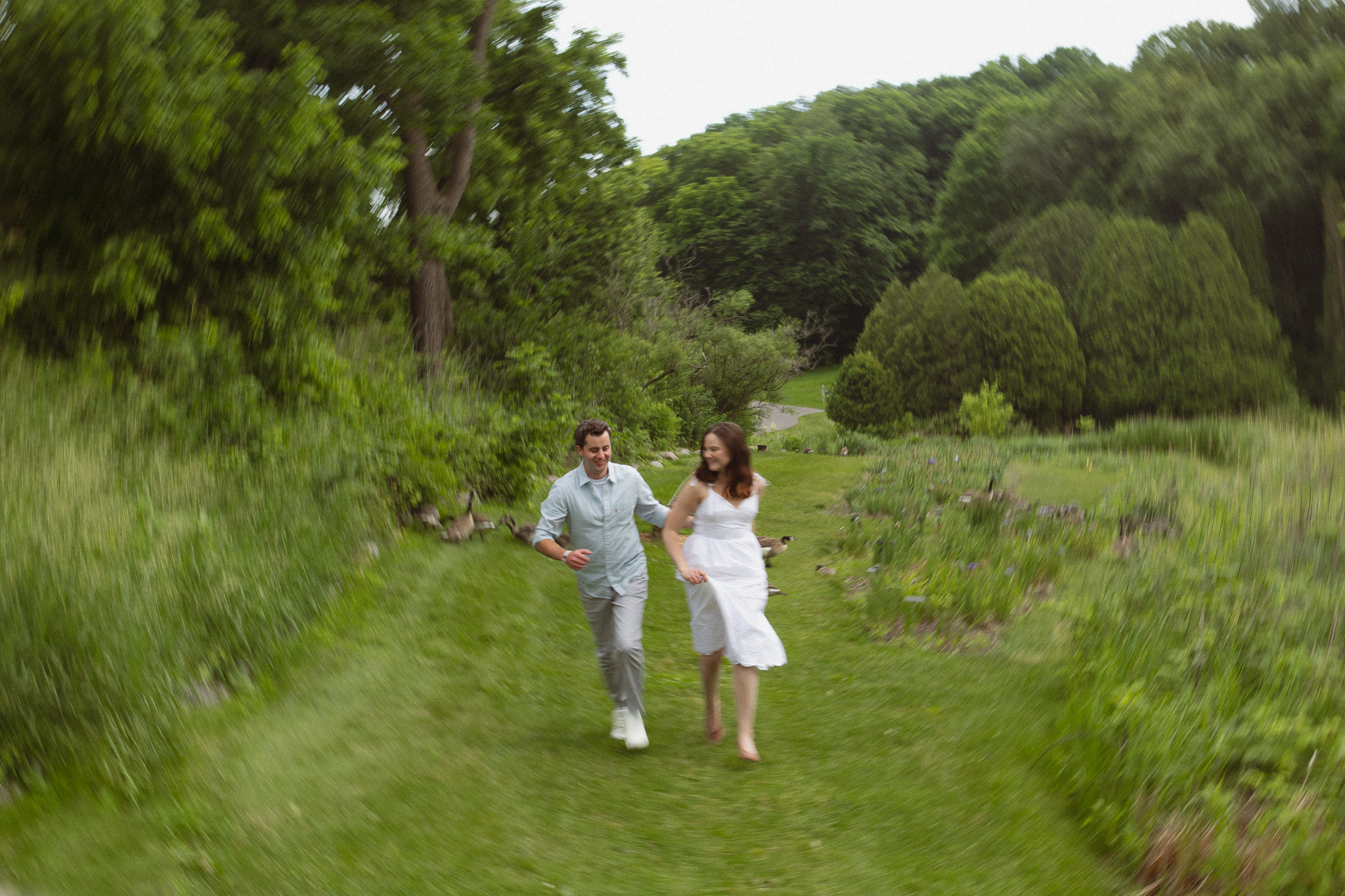Engagement couple running together on grass at the Minnesota Landscape Arboretum