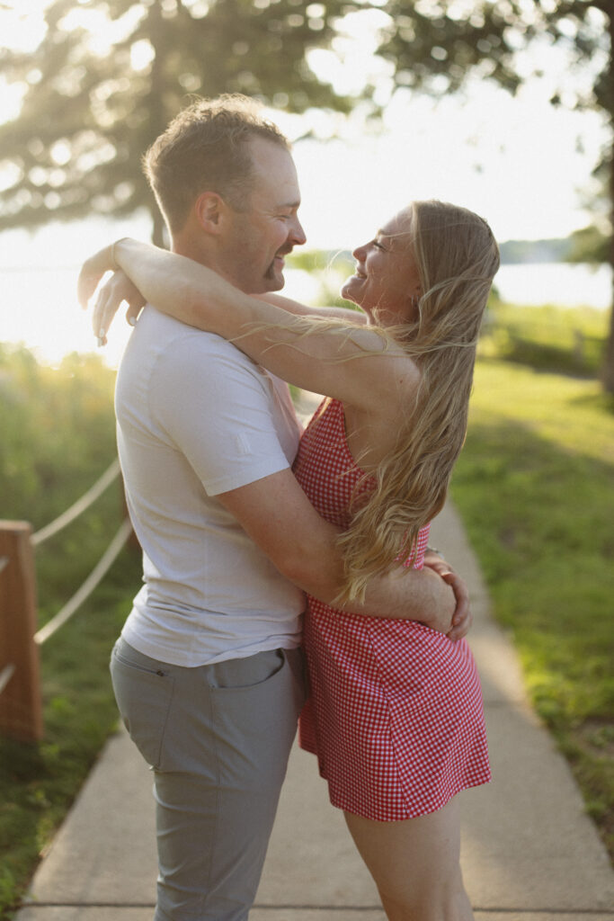 Engagement couple holding each other close laughing as the sun sets behind them over Lake Minnetonka