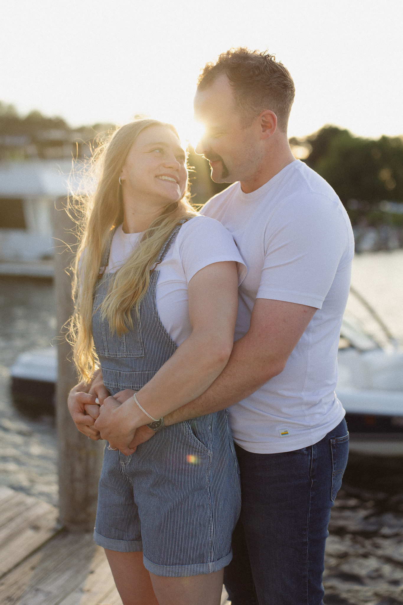 Romantic engagement photo on the dock at Lake Minnetonka in Excelsior during golden hour. The man is holding his girlfriend as the sun sets over Lake Minnetonka
