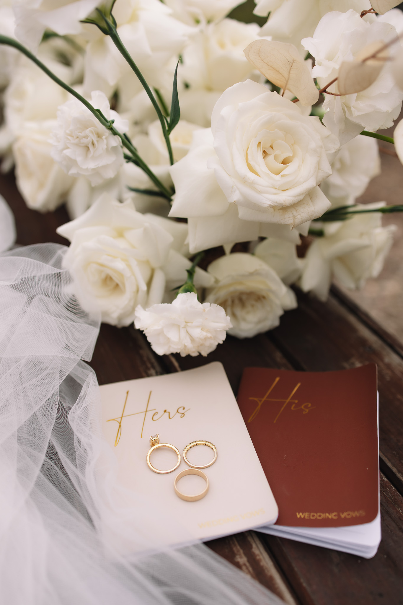 Safari elopement flat lay details- vow books, rings and white rose bouquet