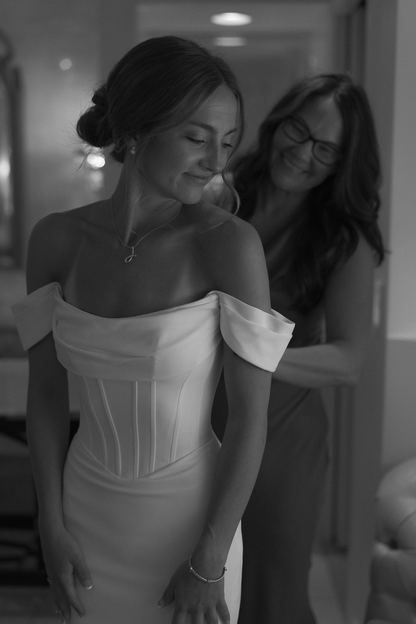 Bride getting ready with her mom who is helping her zip up her dress