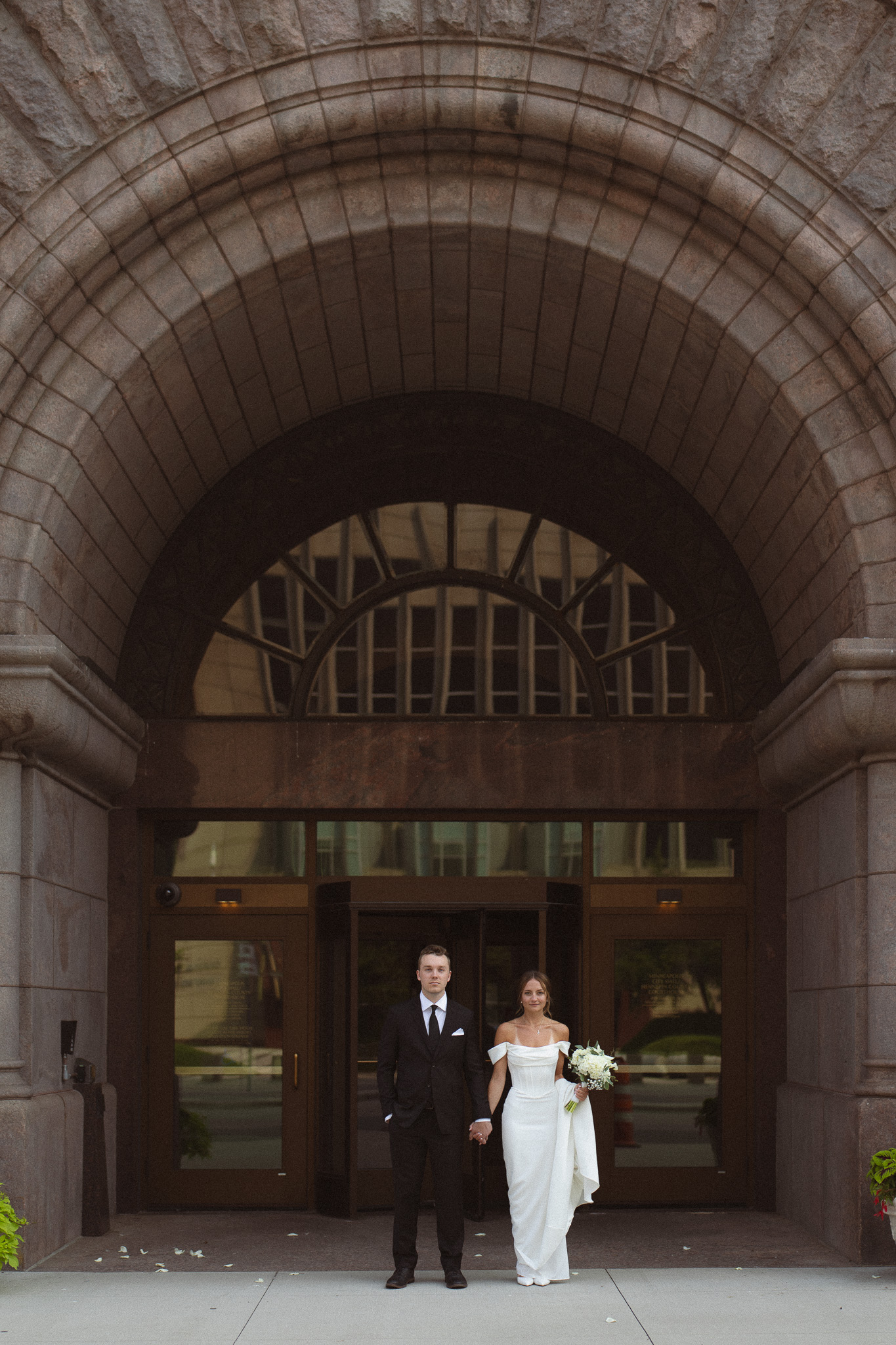 Bride and Groom standing in front of the arched entry way at the Minneapolis City Hall facing opposite directions for a wide shot photo