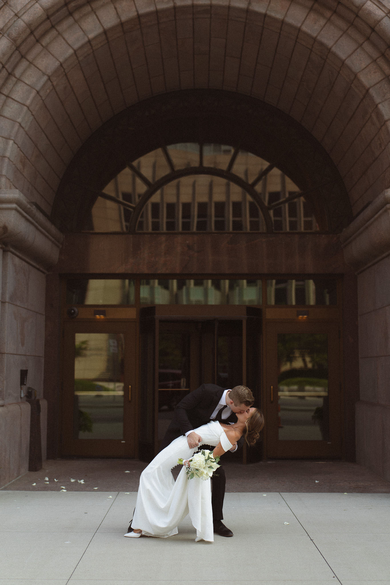 Groom dip kissing his wife in front of the huge archway at the Minneapolis City Hall