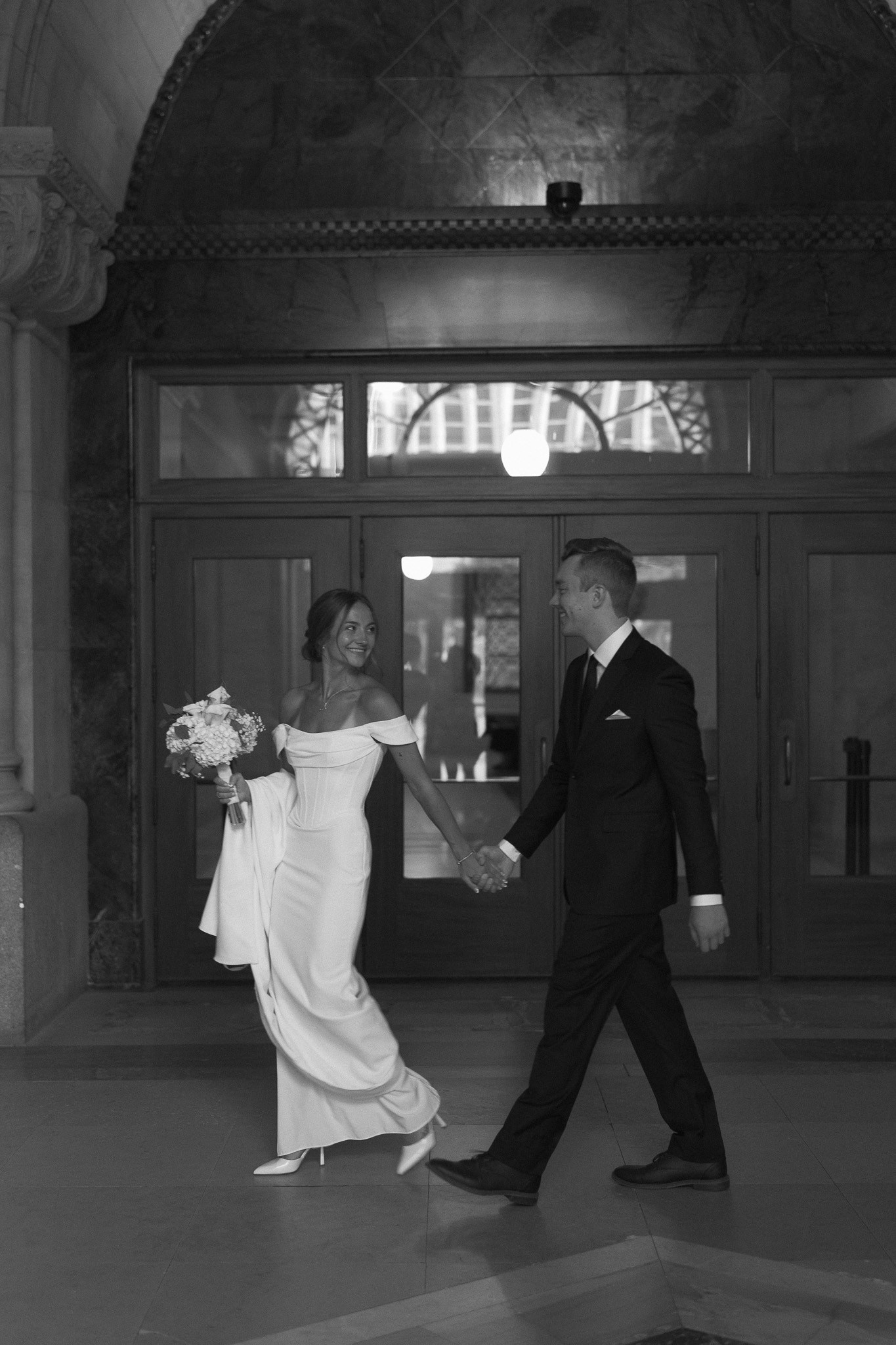 Bride leading Groom down the hallway in front of the big arch inside the Minneapolis City Hall