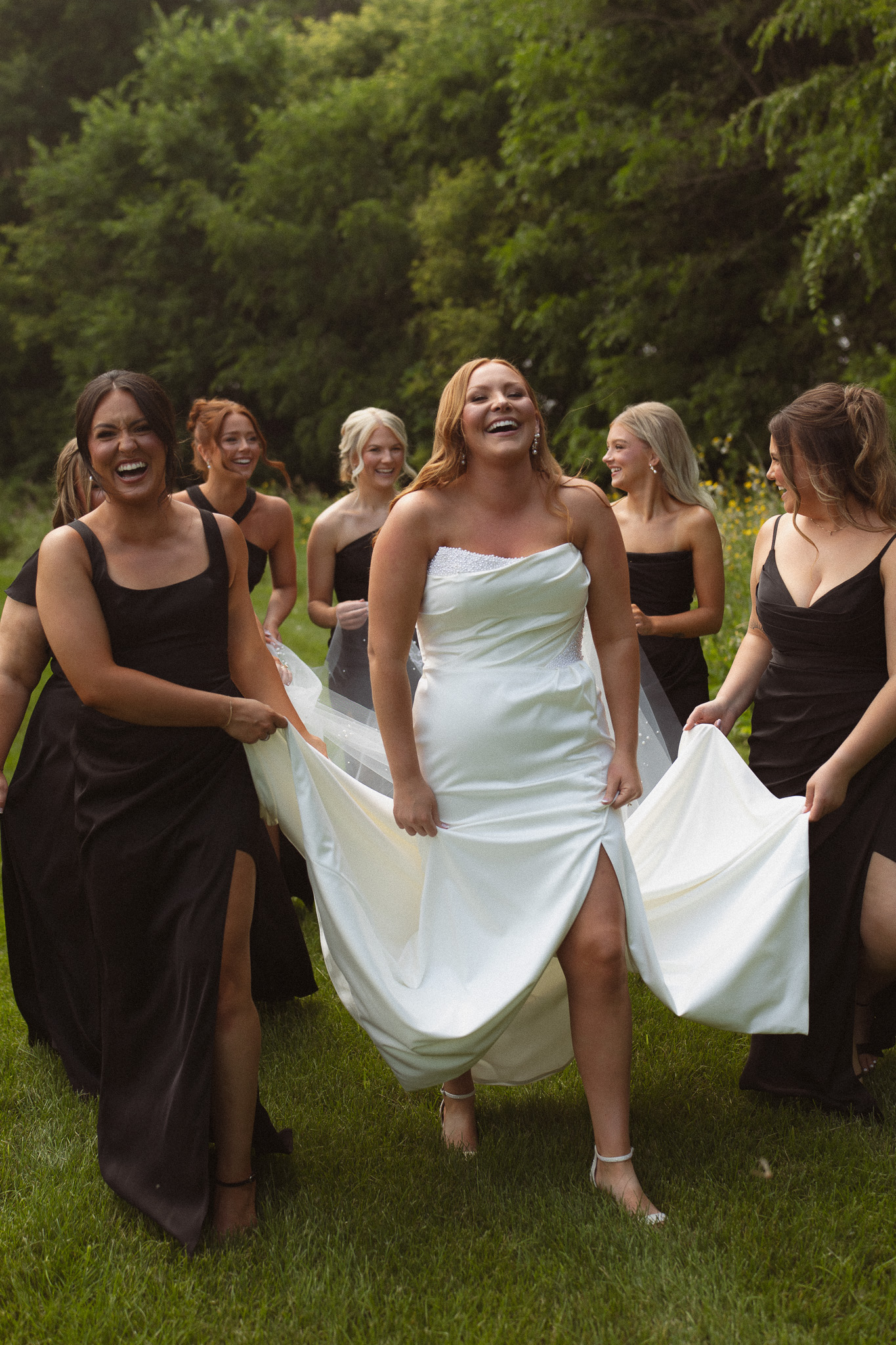 Bridal party helping the bride with her wedding dress as they walk across the grass at The Lafayette Club 