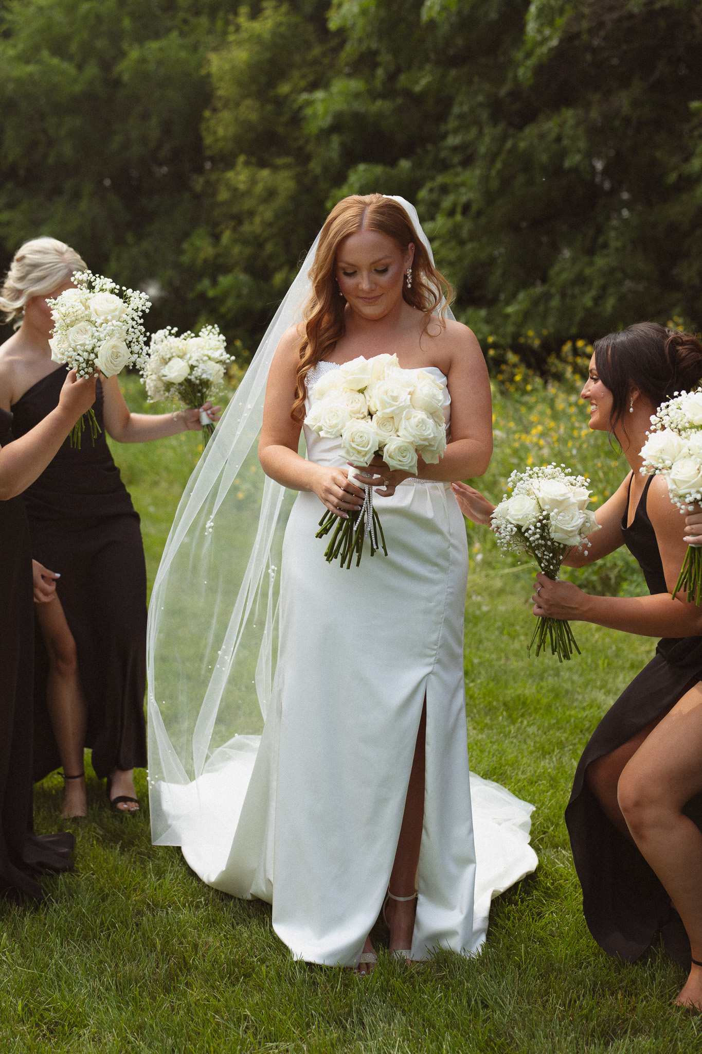 Bride looking down at her bouquet surrounded by her bridesmaids faffing over her
