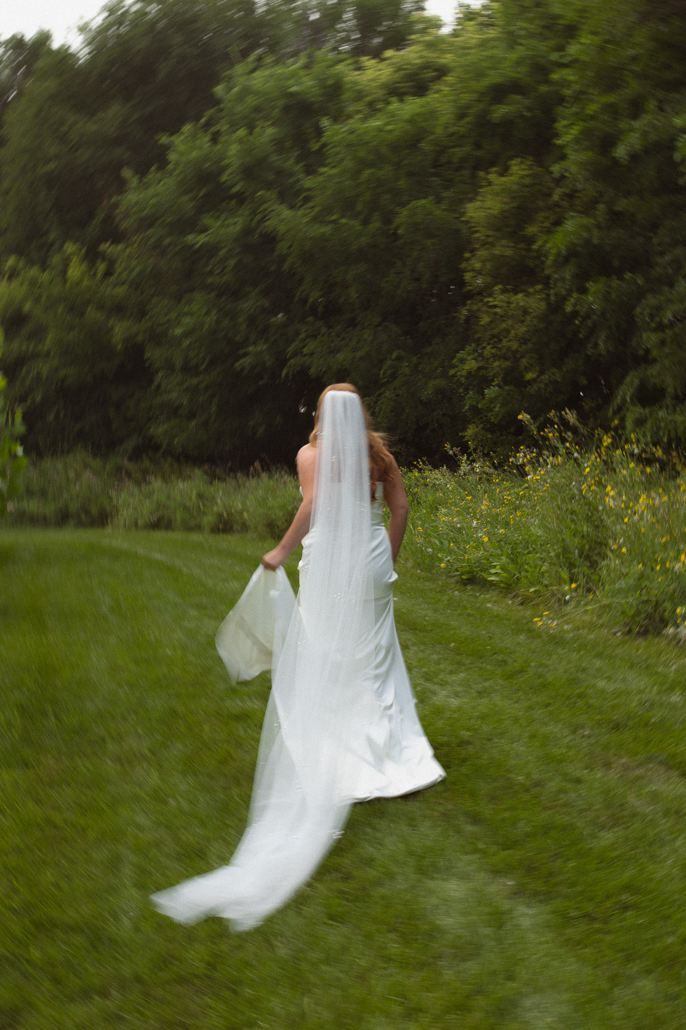 Editorial, documentary, cinematic bridal portrait of bride running in her long white wedding dress across the field at The Lafayette Club in Wayzata