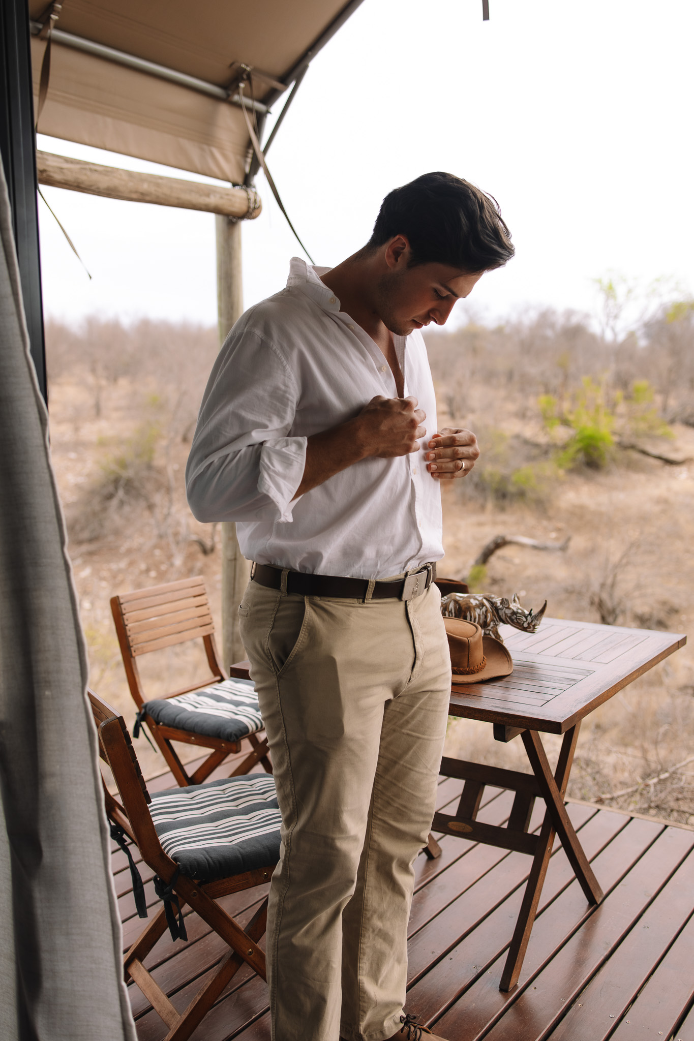 Groom getting ready buttoning his shirt at his safari suite before his safari ceremony and private vows