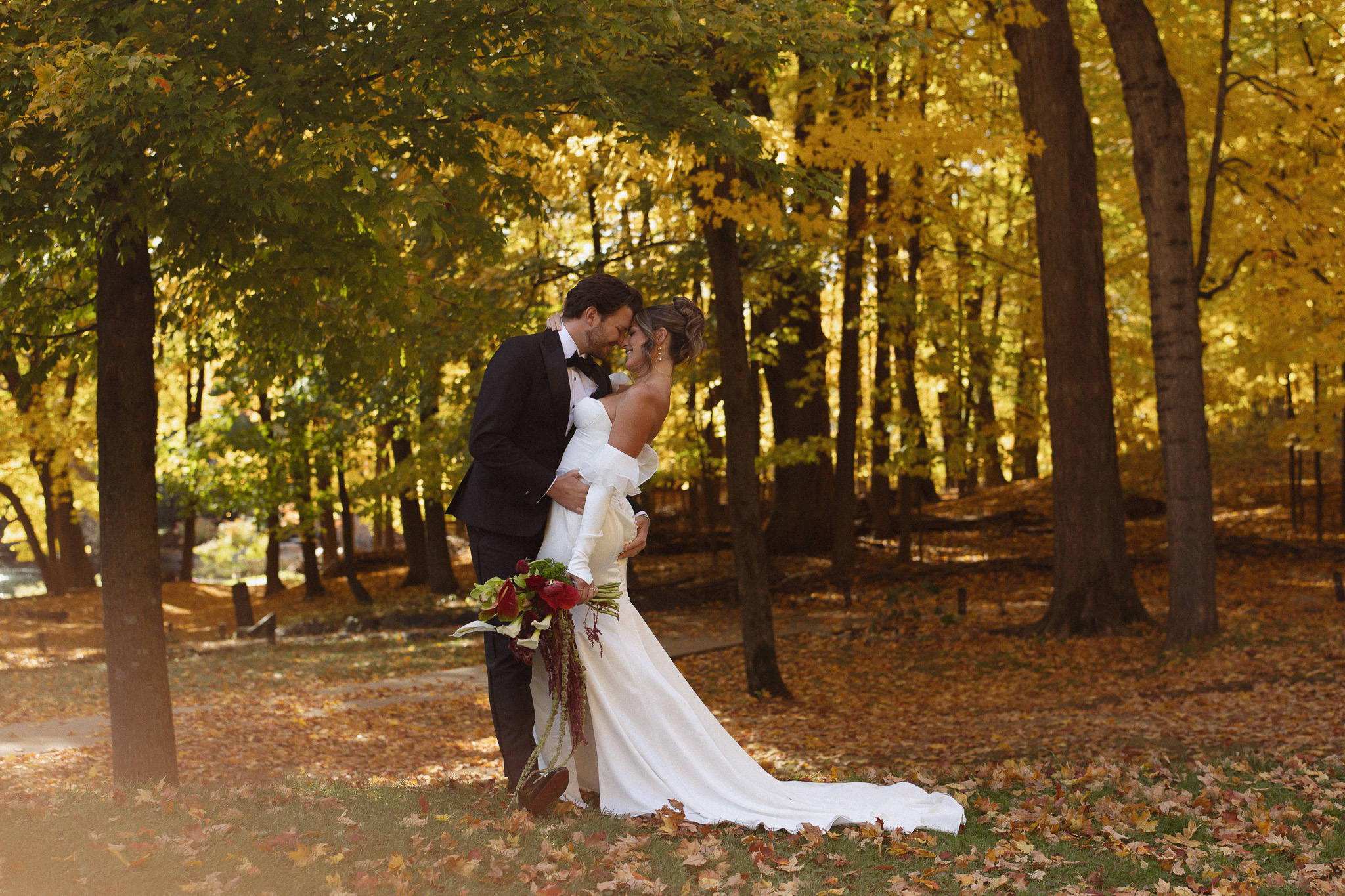 Beautiful landscape photo of bride and groom kissing under the fall trees at The Woods Retreat Wedding Venue in Orono, MN