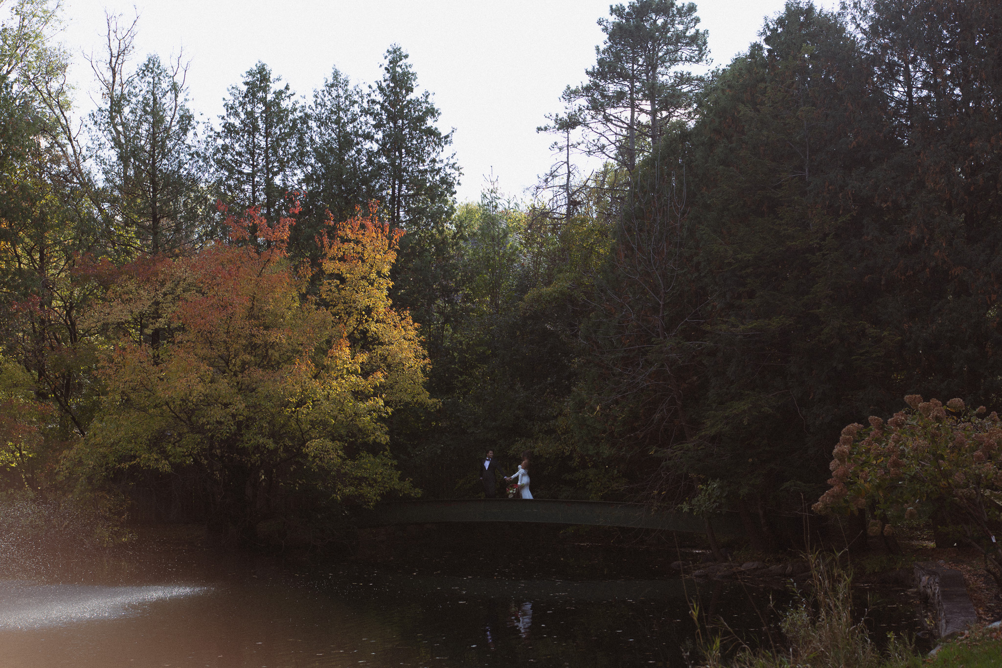 Bride and groom walking across the green bridge stretching over the pond at their woods retreat wedding venue
