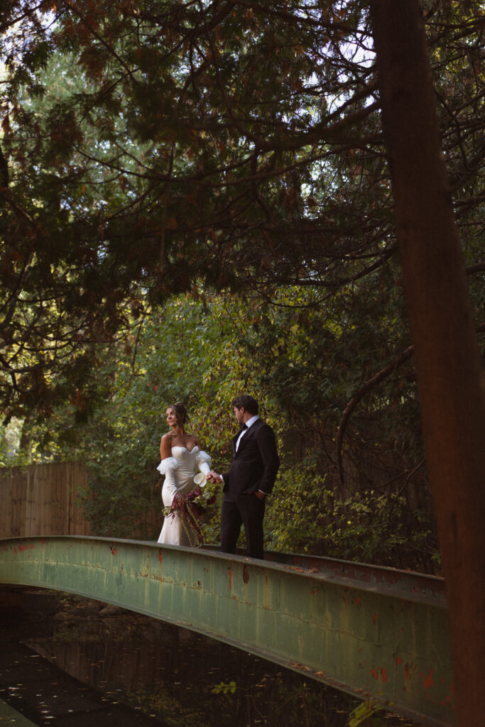 Bride and Groom portraits across the classic green bridge stretching over the pond at the Woods Retreat wedding venue in Orono