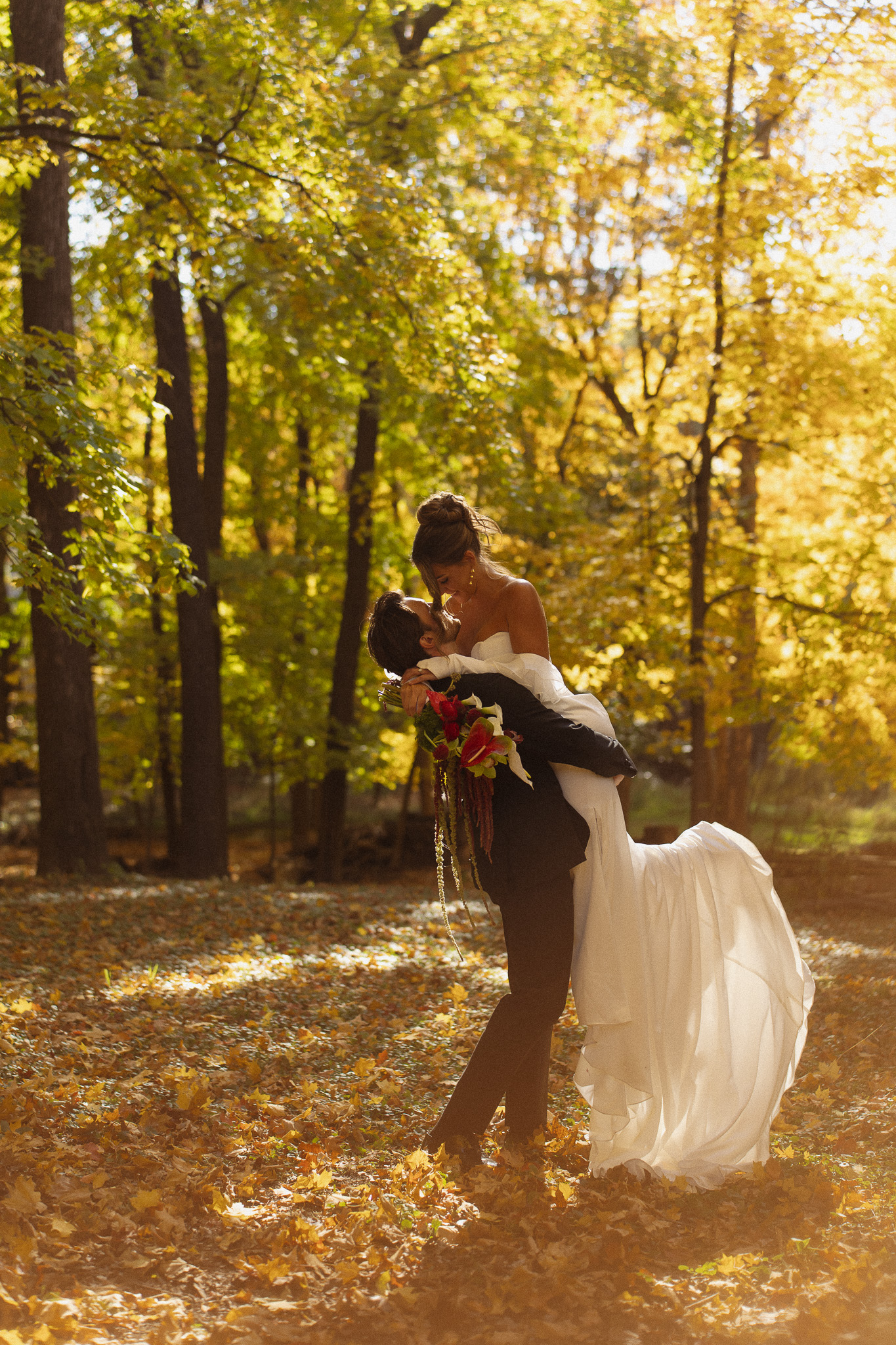 Groom picking up and spinning his bride surrounded by the Fall colors at The Woods Retreat Orono MN wedding