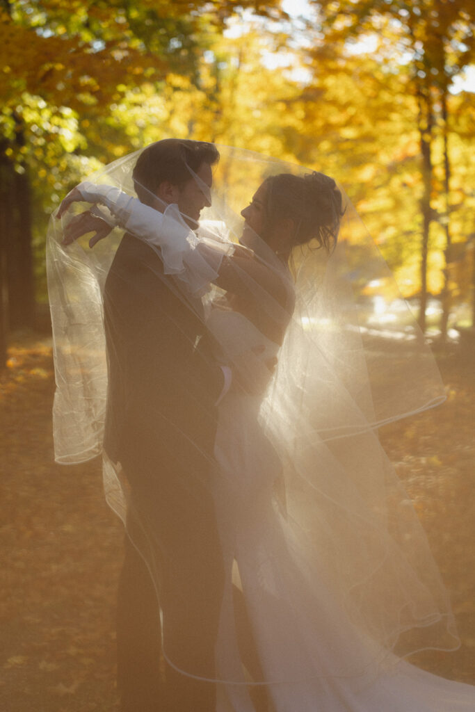 Veil portraits of Bride and Groom at their wedding under the fall trees at The woods retreat wedding in Minnesota