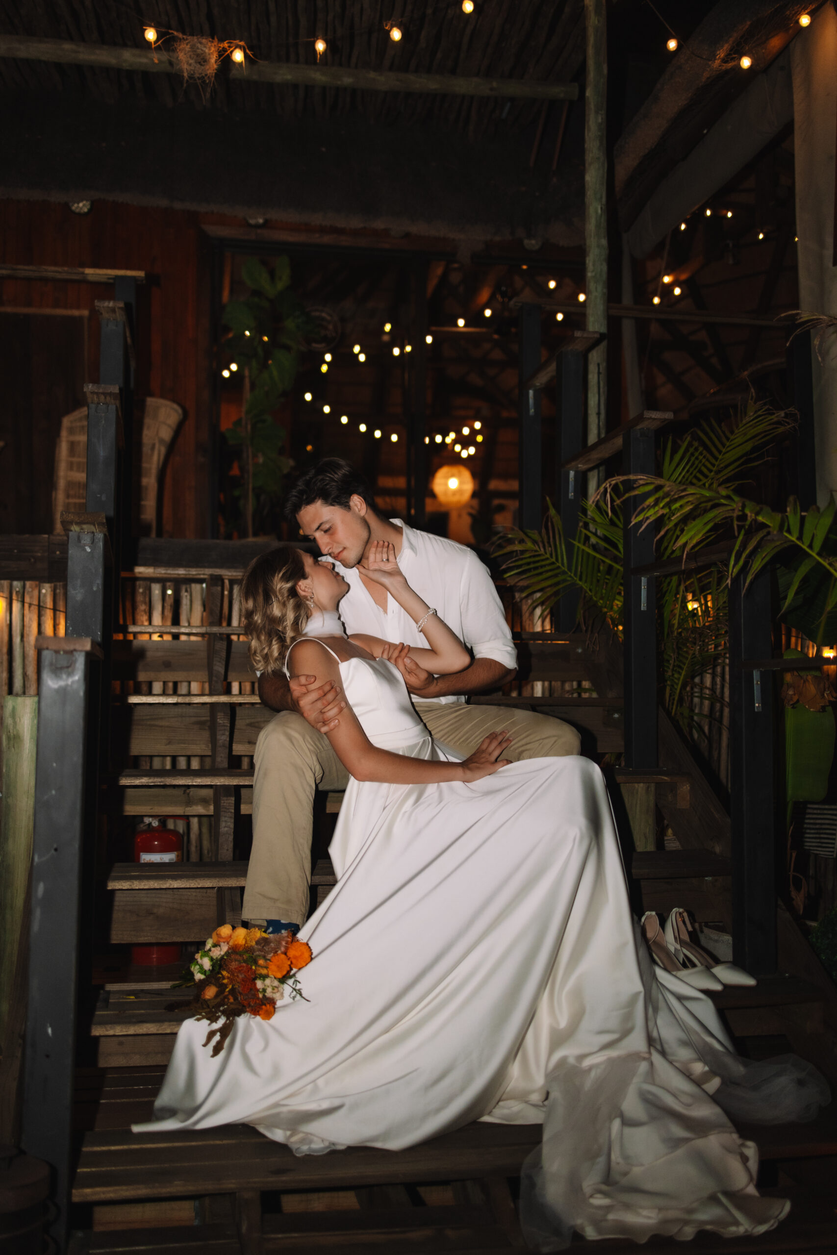 Bride and groom sitting together on wooden steps under warm lights after their safari elopement