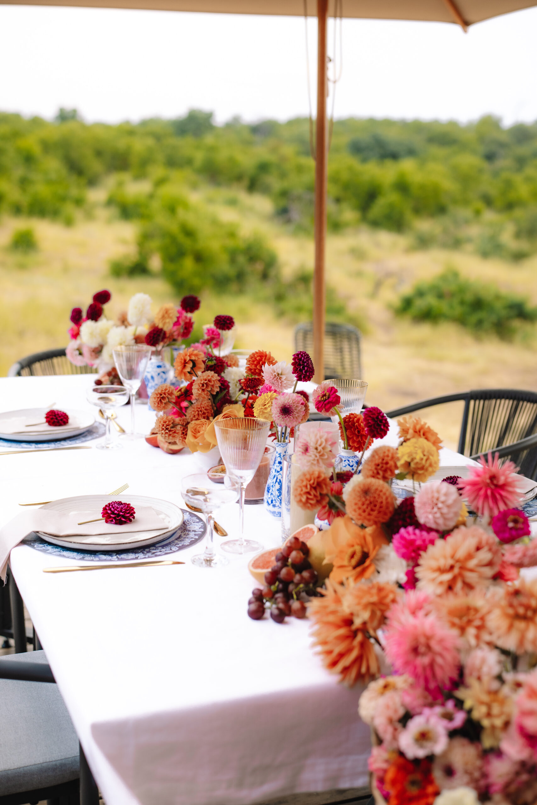 Outdoor safari table styled with colorful florals, glassware, and place settings overlooking the bush