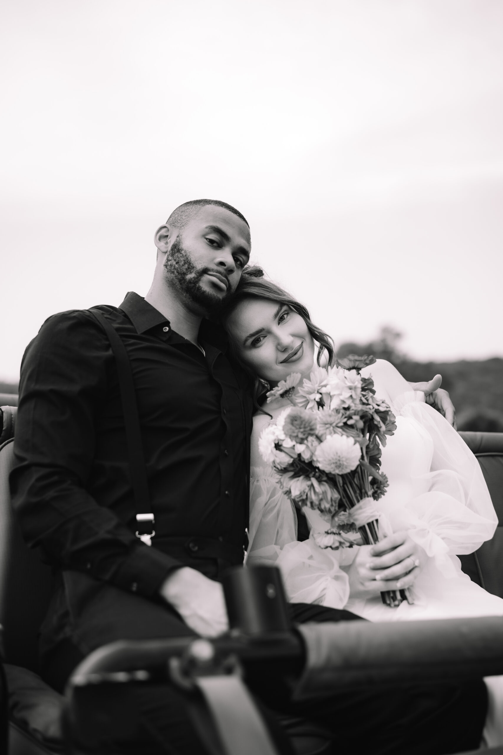 Black and white portrait of newlyweds leaning together in an open safari vehicle