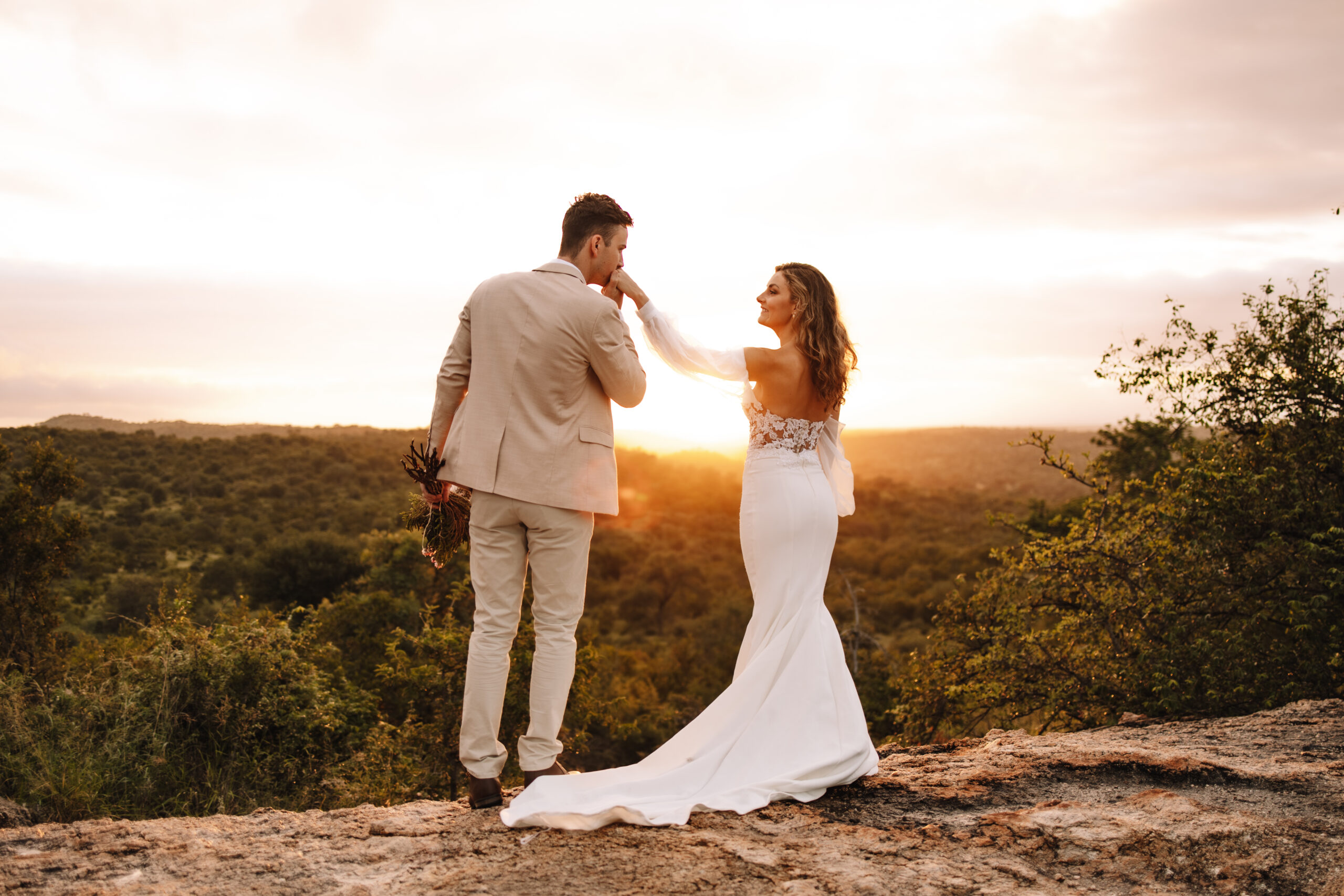 Bride and groom standing on a cliff at sunset overlooking the African bush on a luxury safari elopement