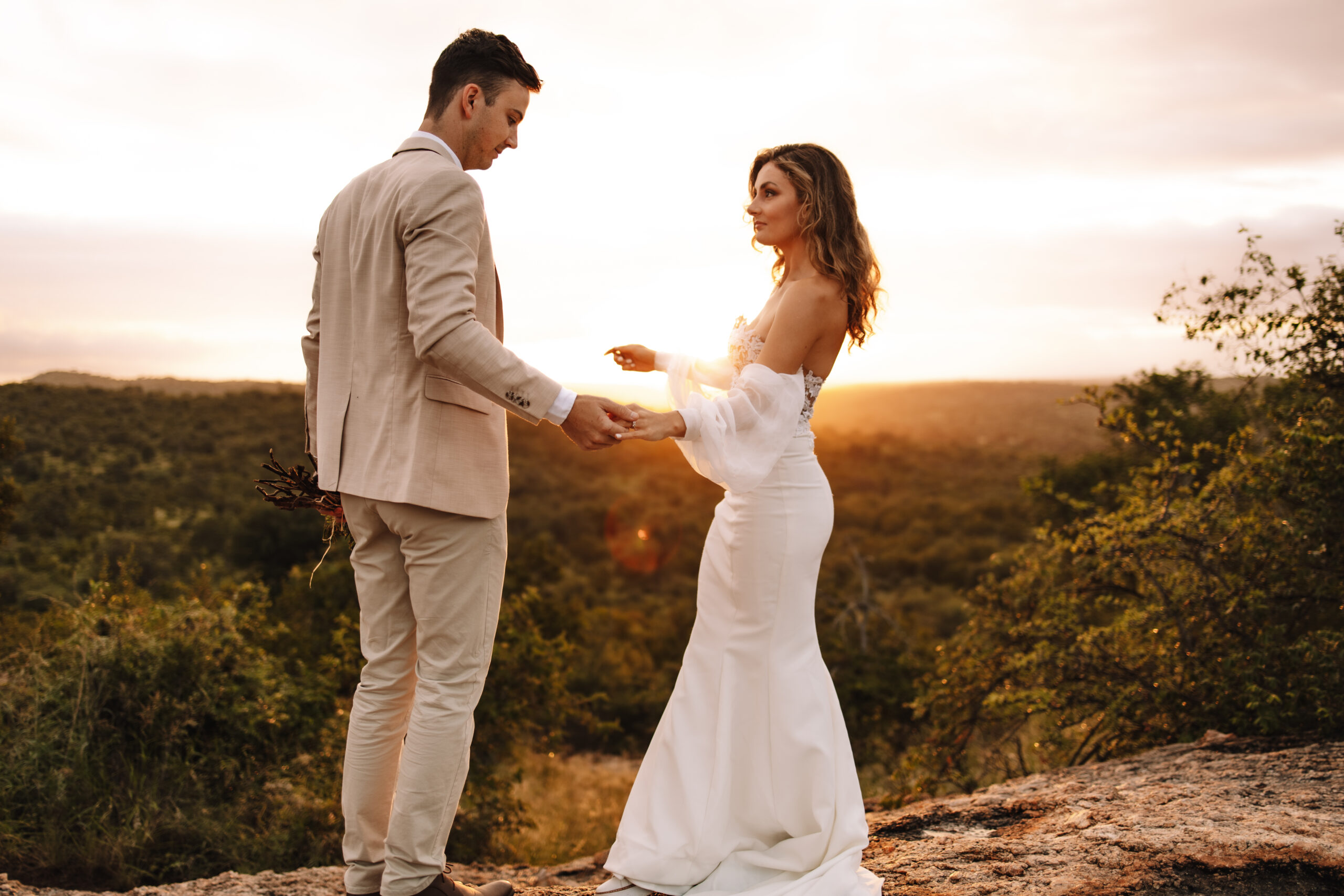 Bride and groom holding hands on a rocky overlook at sunset during a luxury South Africa safari wedding
