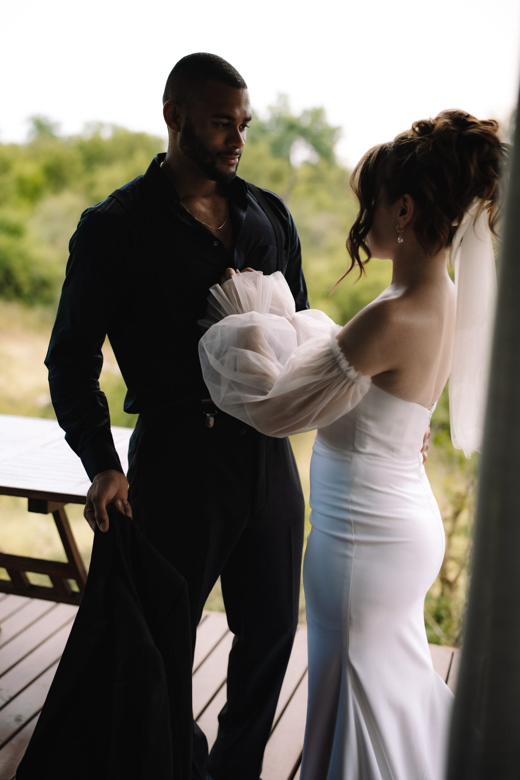 Bride adjusting the groom’s sleeve on a lodge deck before their safari elopement in South Africa