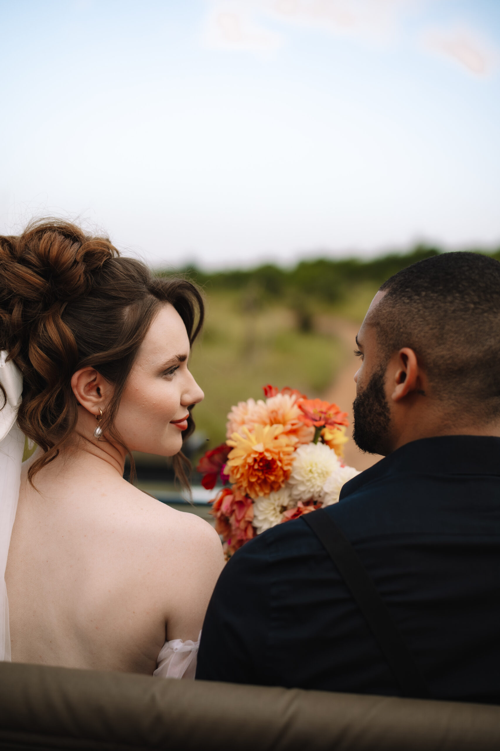 Bride and groom sitting together in a safari vehicle holding a bouquet during game drive
