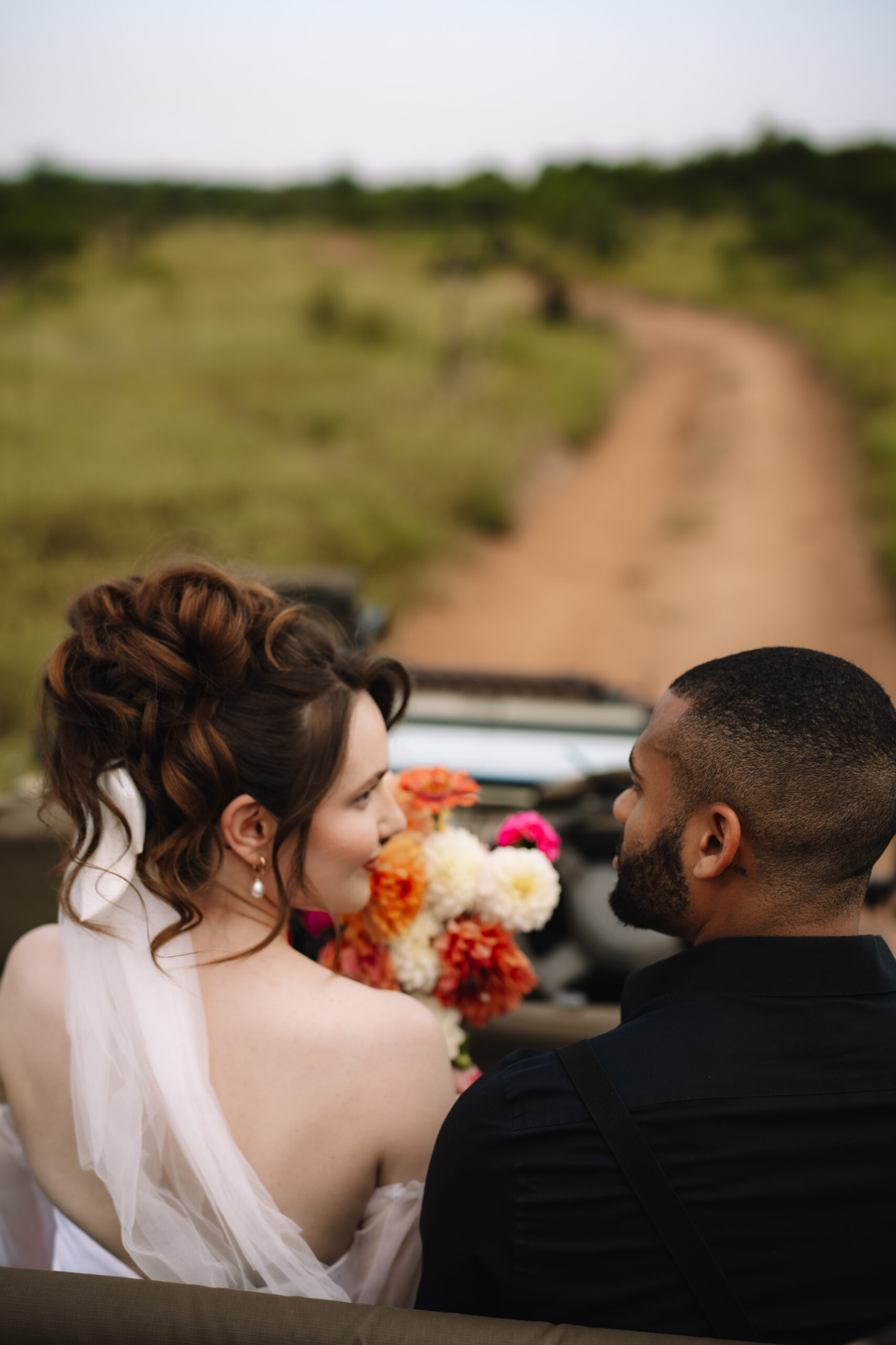 Bride and groom looking at one another while sitting in open safari vehicle