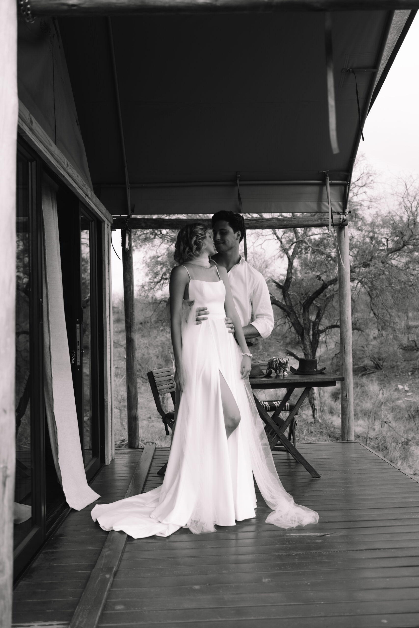 Black and white portrait of a couple standing together on a lodge deck overlooking the bush