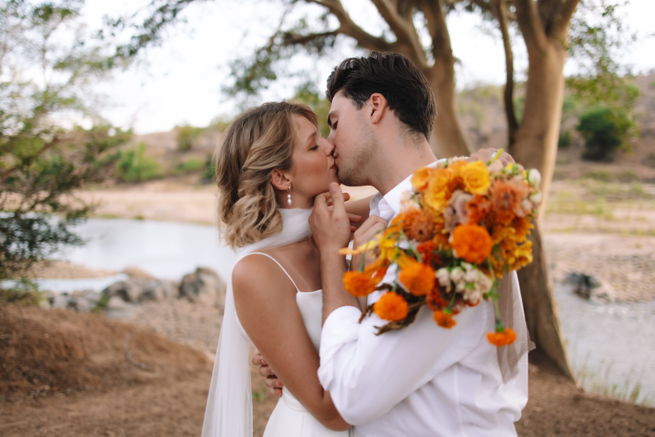 Couple sharing a kiss near a riverbank after exchanging vows during a safari elopement in South Africa