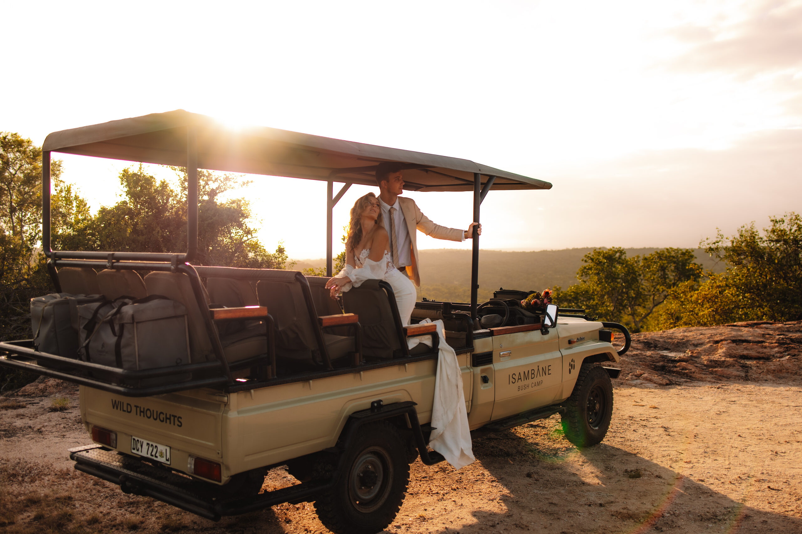 Couple standing together in an open safari vehicle at sunset overlooking the bush