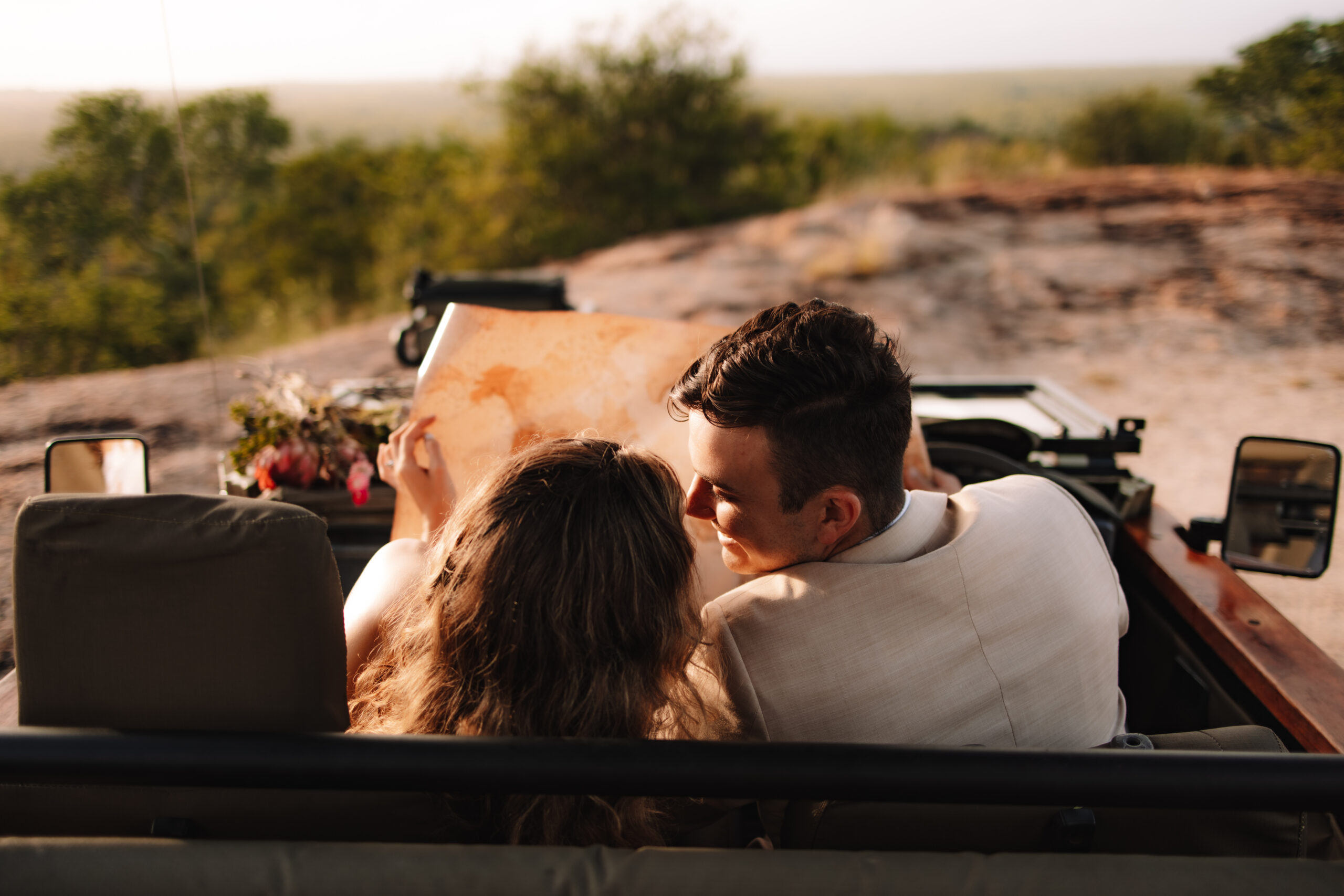 Newlywed couple sitting together in an open safari vehicle during golden hour game drive