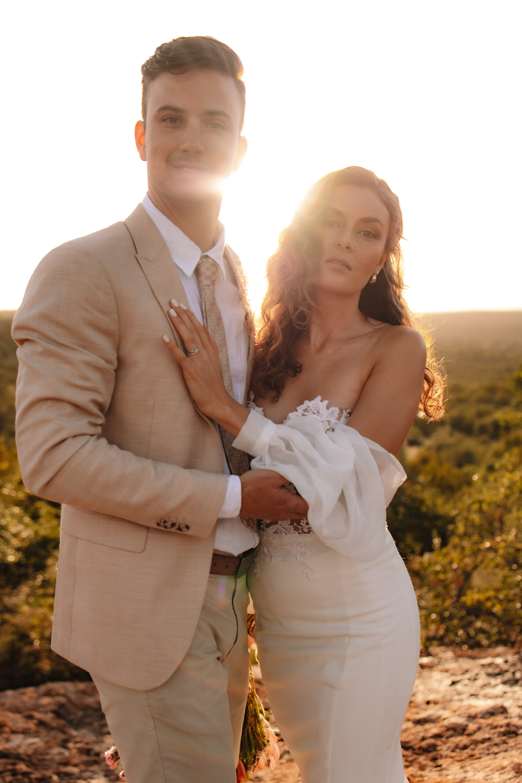 Bride and groom standing close together with sunlight behind them on a scenic overlook