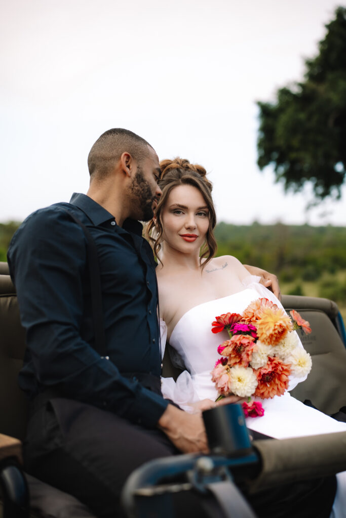 Bride and groom seated together in a safari vehicle, cuddling with a colorful bouquet during their wedding in a Private Game Reserve in South Africa.