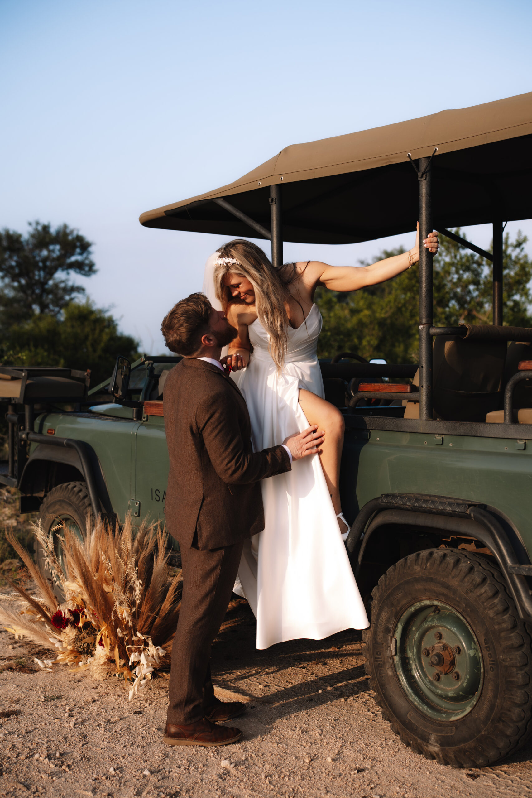 Groom helping his bride down from a safari vehicle while they laugh together during their wedding day adventure.