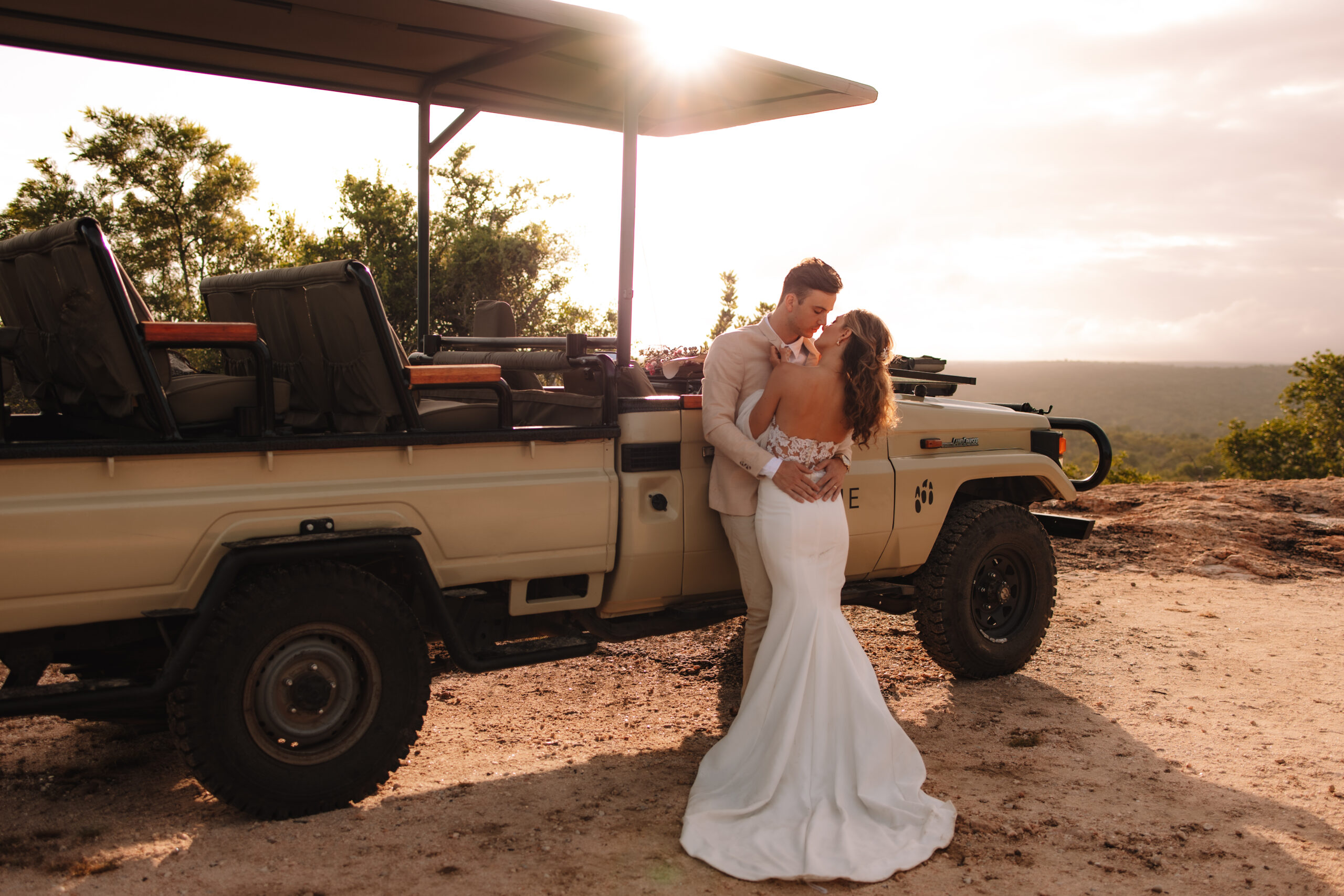 Bride and groom kissing beside a safari vehicle at sunset during their wedding at a Private Game Reserve in South Africa, with golden light and sweeping views.