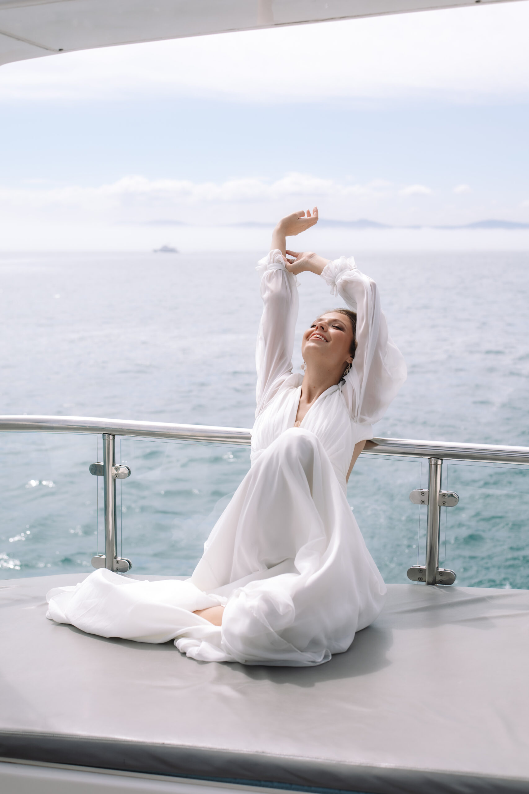 Bride relaxing barefoot on the deck of a yacht during a Cape Town elopement, her flowing dress catching the breeze with calm ocean views beyond.